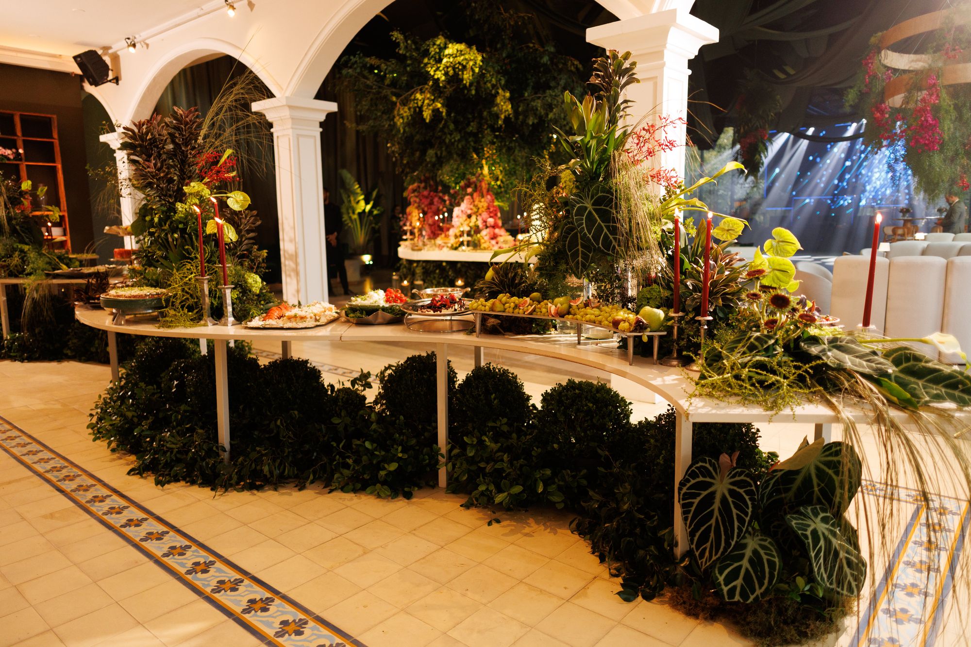 Buffet com frutas, velas vermelhas e arranjos tropicais no salão