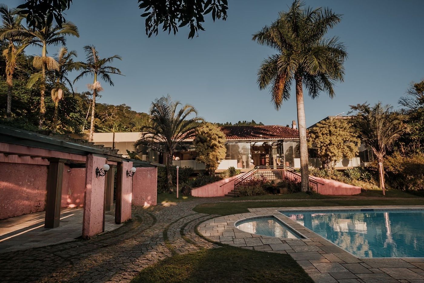 Casarão rosa ao entardecer com a piscina iluminada