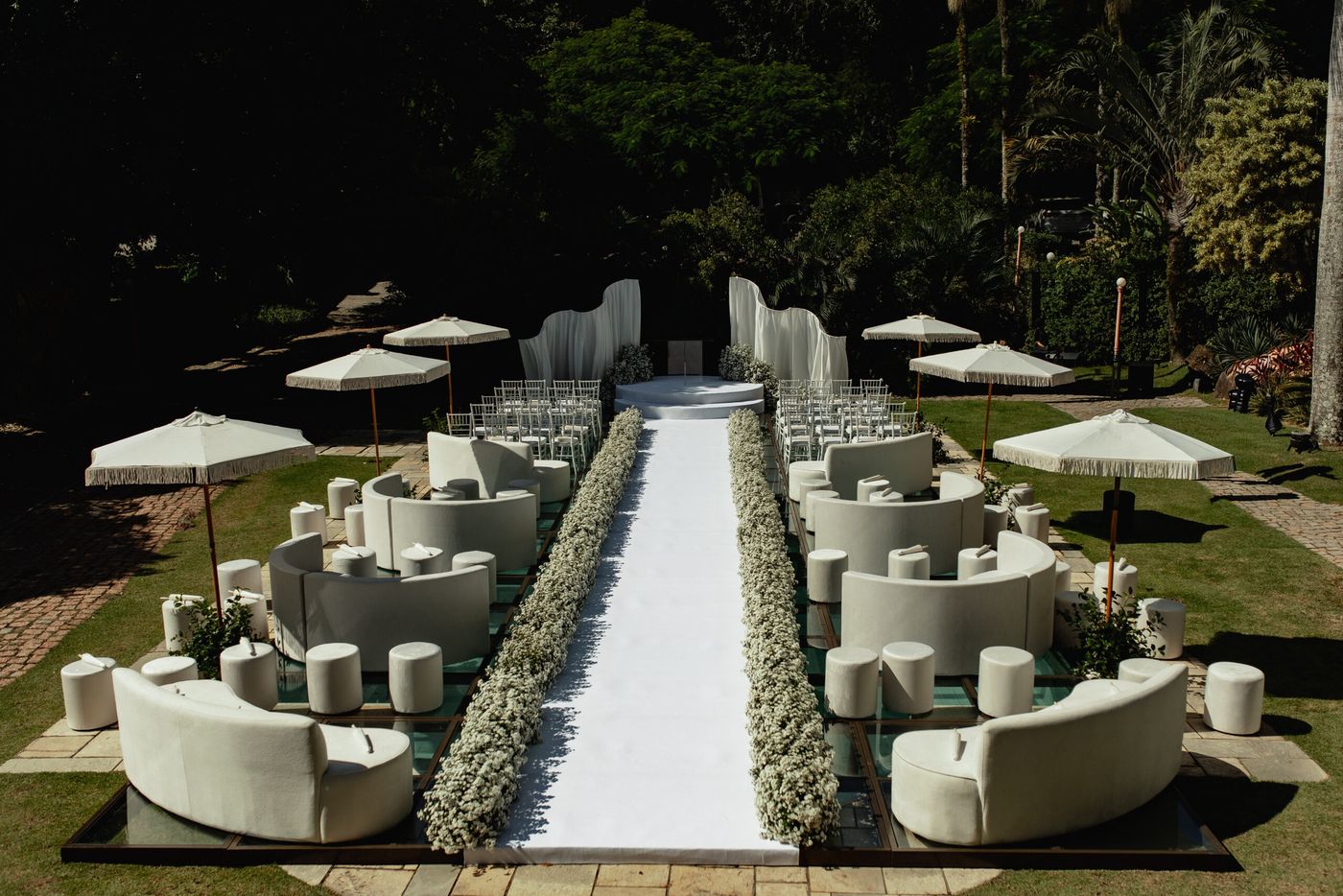 Corredor branco da cerimônia no jardim com lounges e ombrelones