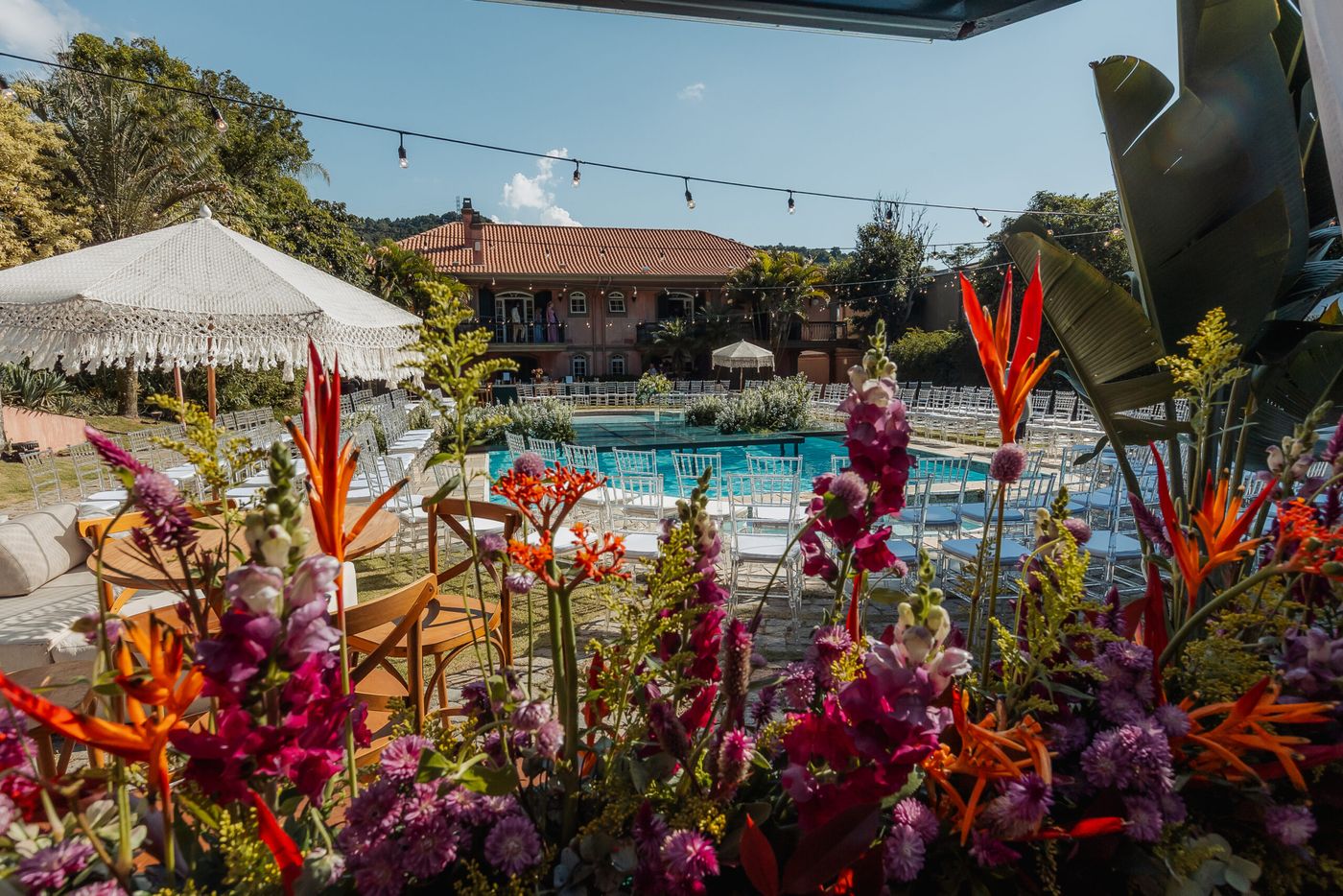 Flores coloridas em primeiro plano com a piscina e o casarão ao fundo